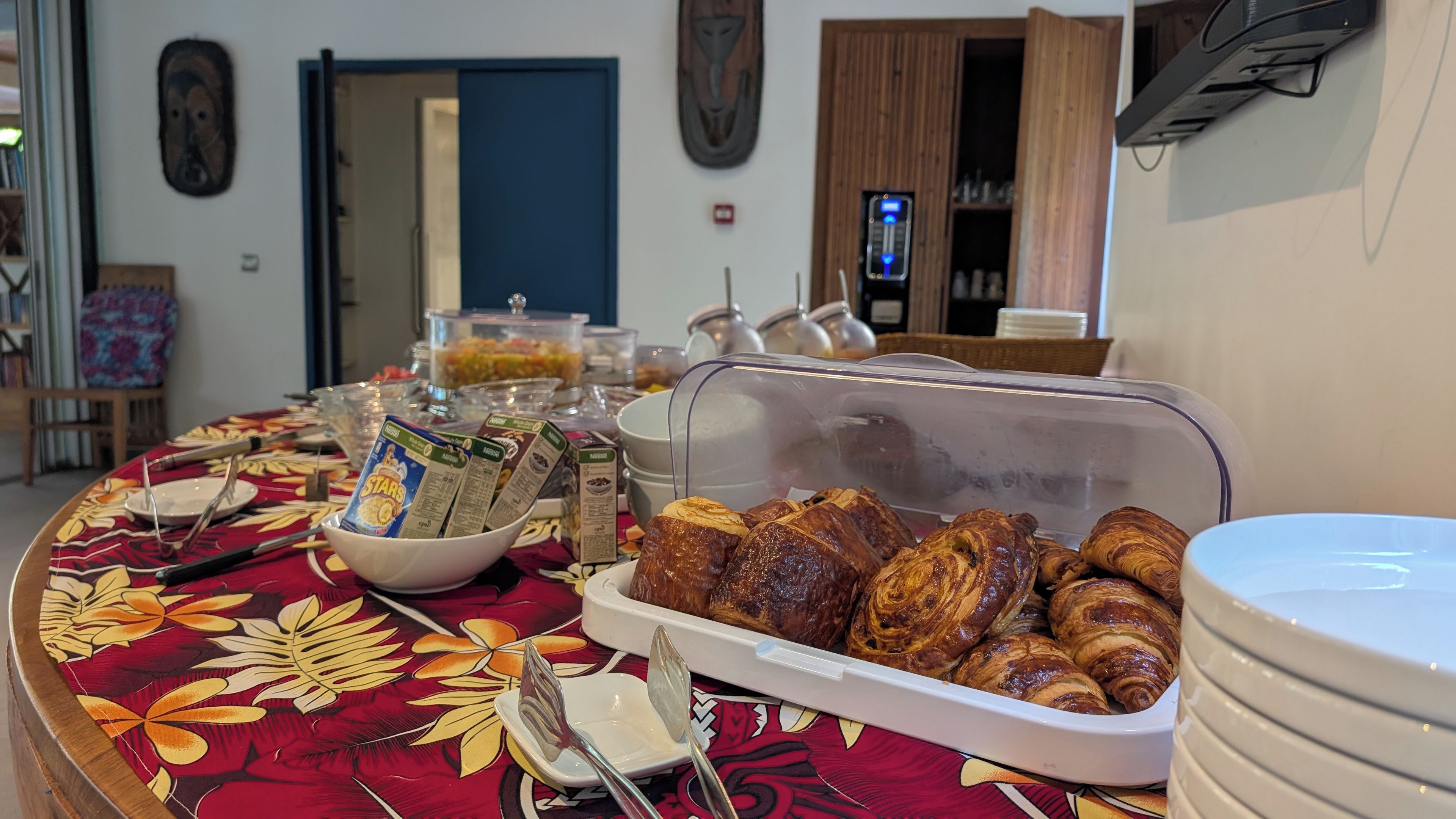Mesa de buffet con alimentos, incluyendo pasteles y bebidas, en una habitación con puerta y adornos en la pared.