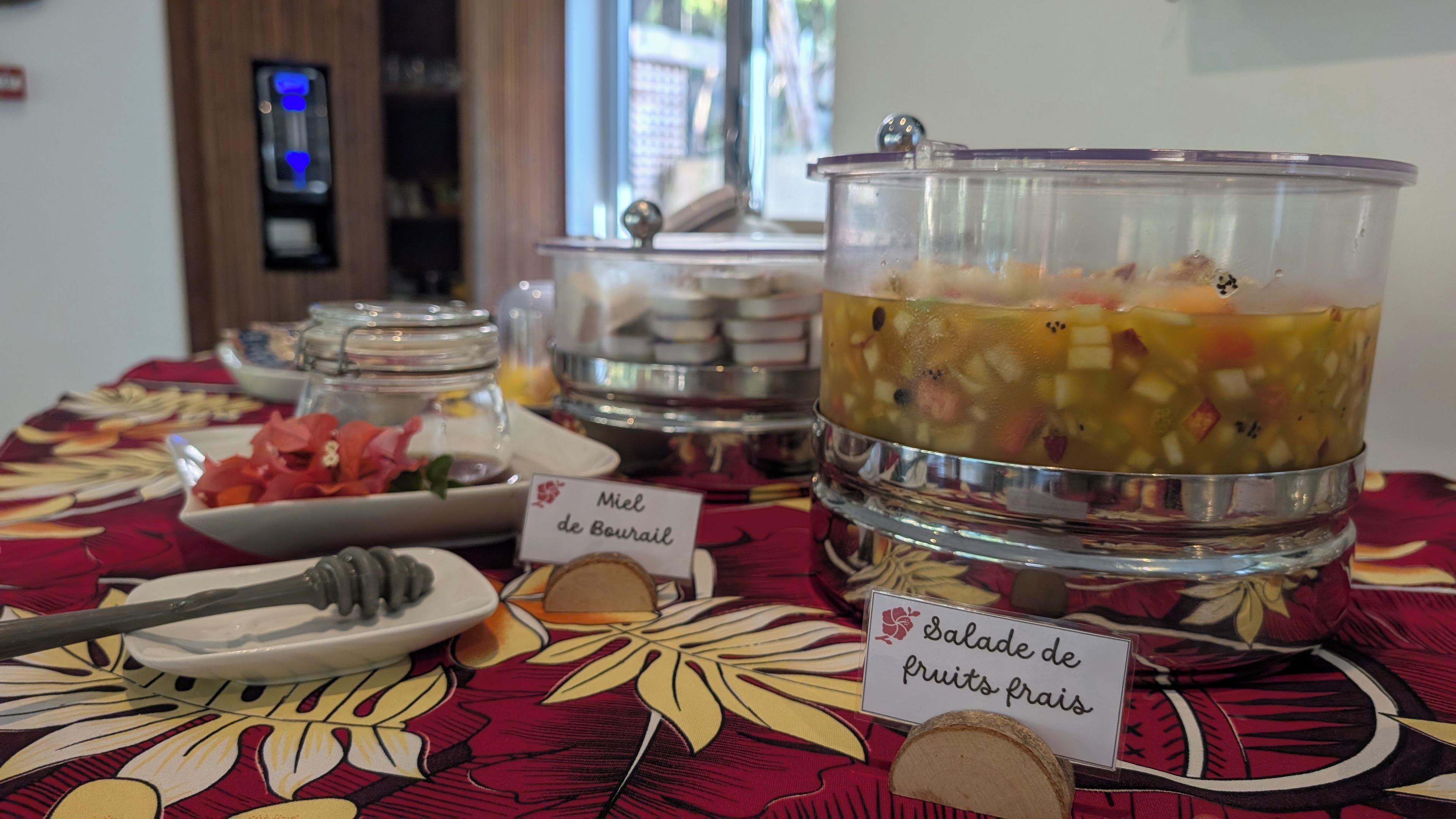 A buffet table with labeled dishes including 'Miel de Bourbon' and 'Salade de fruits frais'.