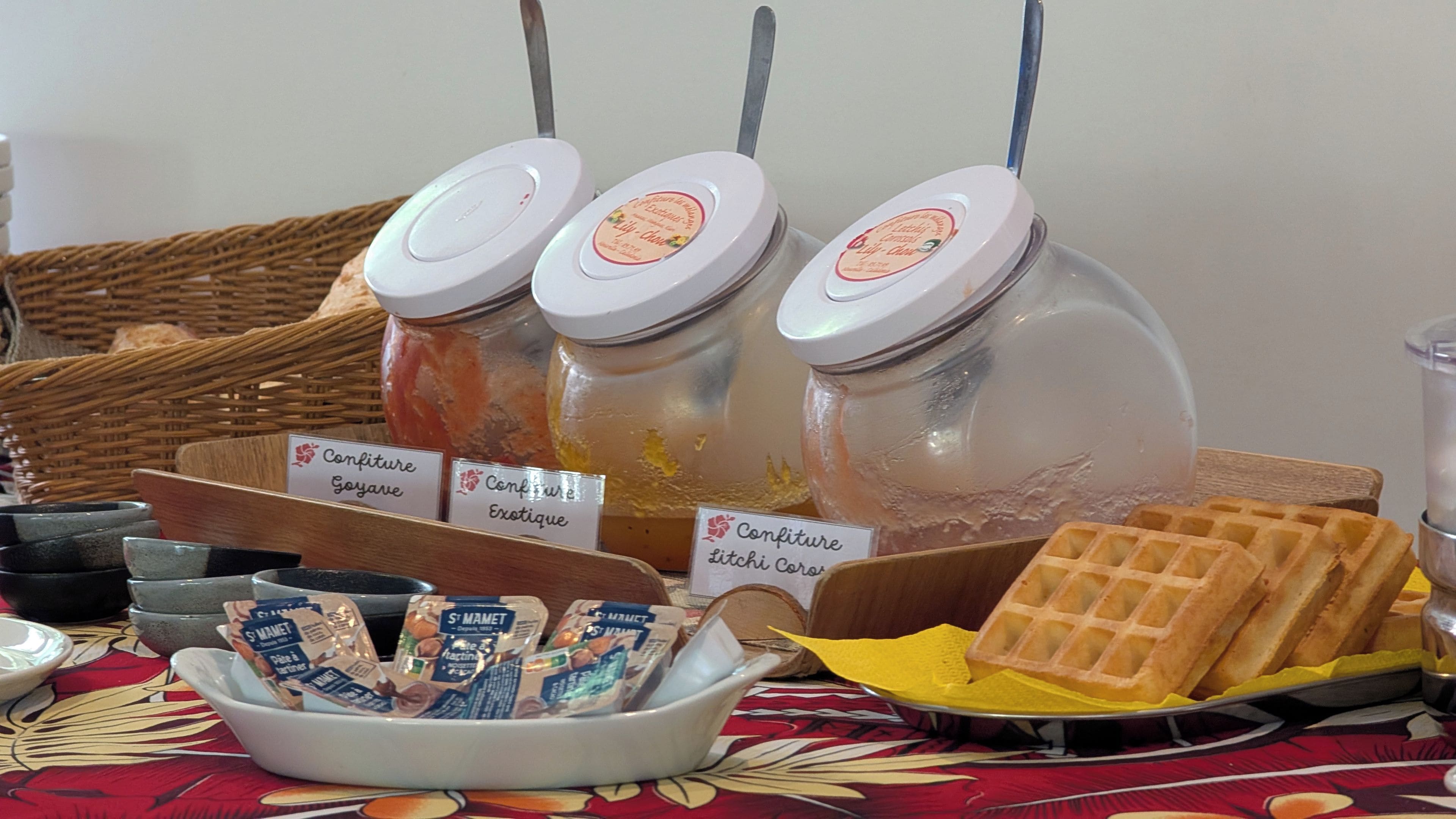 A breakfast buffet with labeled jars of spreads, a bowl of packaged snacks, and a tray of waffles.