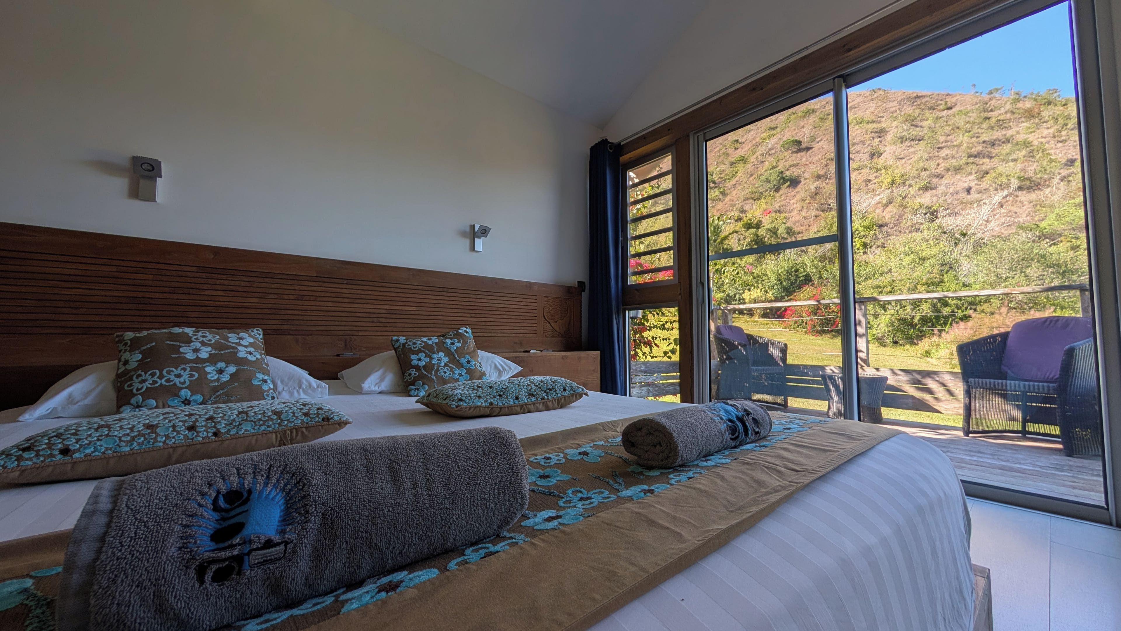 A bedroom with a large bed, a wooden headboard, and a view of a hillside through a sliding glass door.