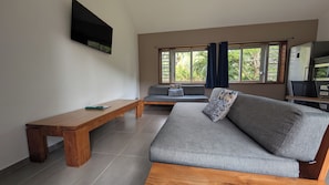 Una sala de estar con un sofá, un banco de madera y un televisor montado en la pared.
