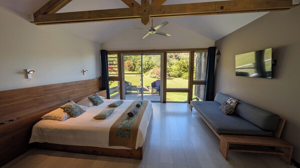 A bedroom with a bed, a sofa, a ceiling fan, and a TV.
