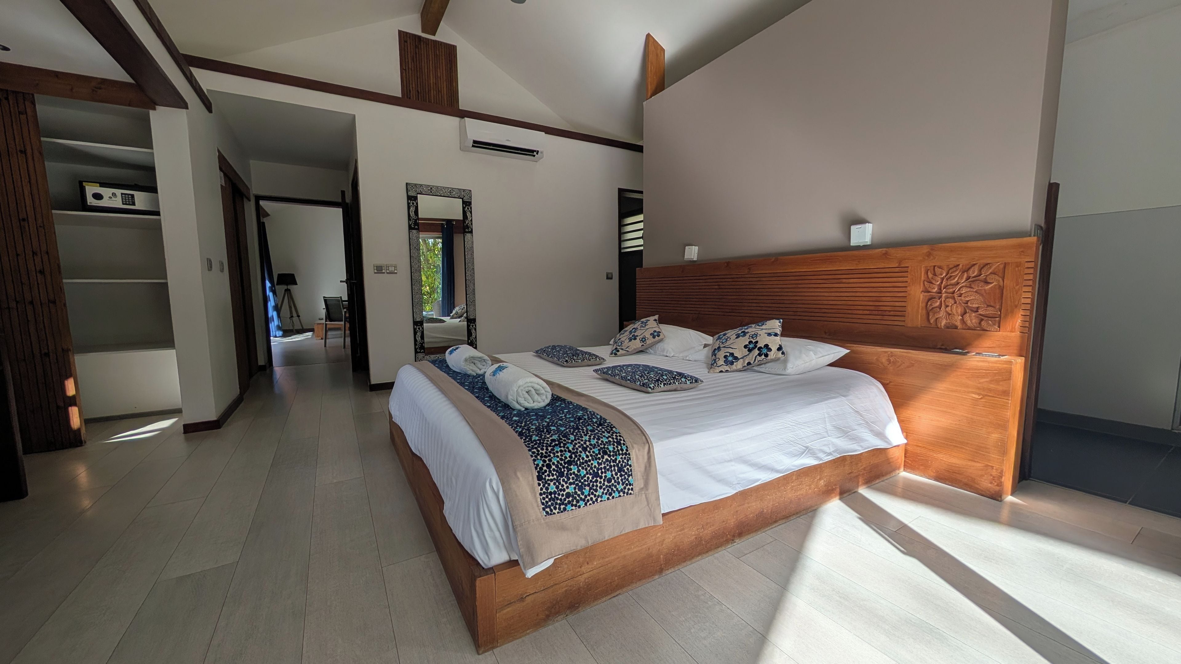Une chambre spacieuse avec un grand lit, une tête de lit en bois et un dressing.