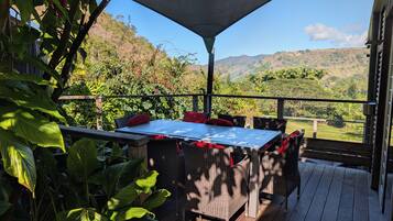 Un espace de restauration en plein air, avec une table et des chaises, entouré d’une végétation luxuriante et offrant une vue sur les collines.