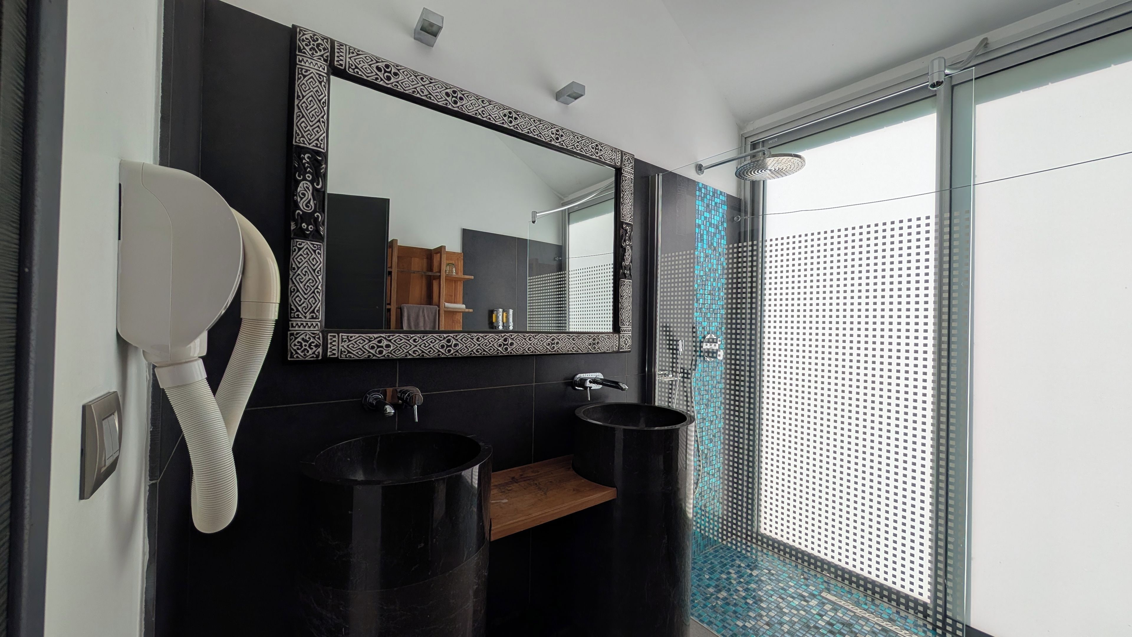 Ein modernes Badezimmer mit einem schwarzen Waschbecken, einem Spiegel mit dekorativem Rahmen und einer Duschkabine mit Glastür.