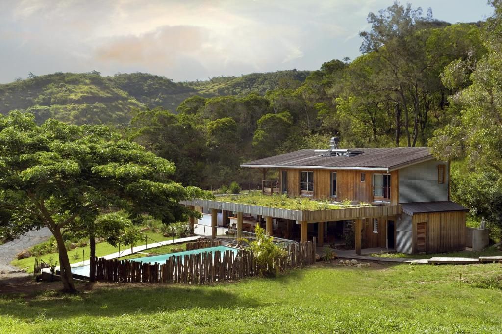 A modern house with a flat roof, a swimming pool, and a lush green landscape.