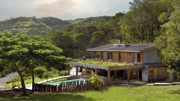 A modern house with a flat roof, a swimming pool, and a lush green landscape.