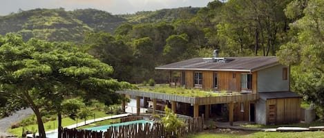 A modern house with a flat roof, a swimming pool, and a lush green landscape.