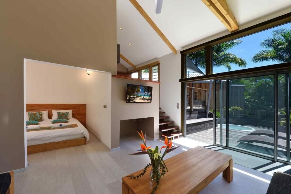Un dormitorio moderno con cama, una mesa de centro de madera y vistas a una piscina a través de amplios ventanales.