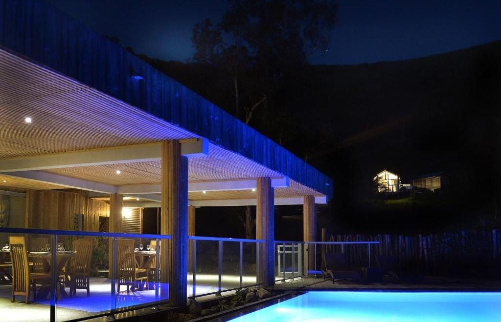 Ein modernes Haus mit Pool, großen Fenstern und einer überdachten Terrasse.