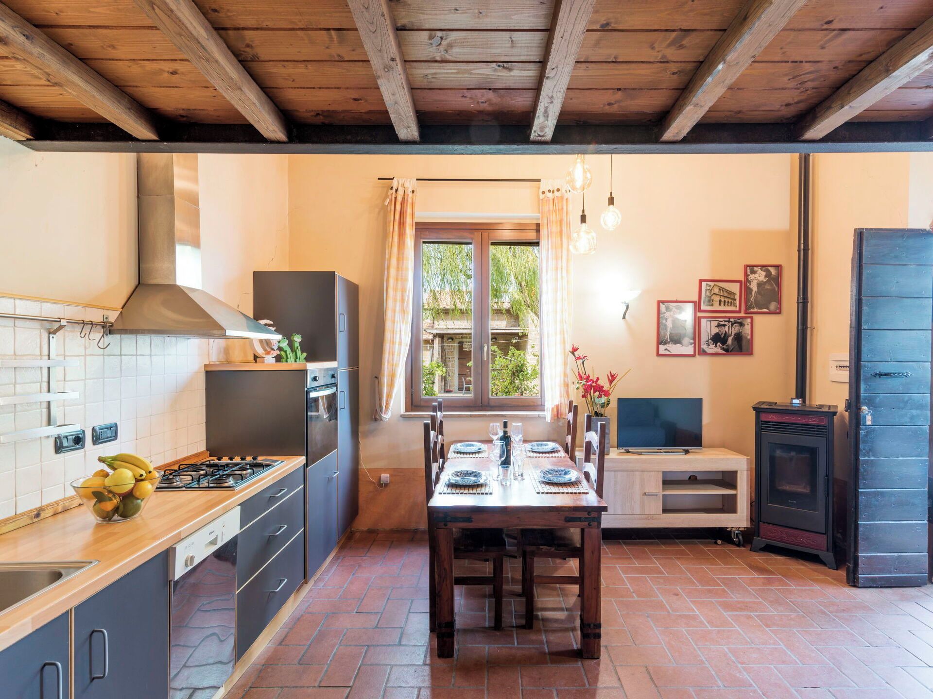 A kitchen with a stove, oven, and sink; a dining table with chairs; a window with curtains; a stove; and a door.
