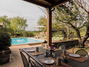 A poolside area with a table set for two, a chair, and a view of the pool and surrounding greenery. - Lovely apartment in villa with hot tub, pool, WIFI, TV, patio, pets allowed and panoramic view (Montefiascone)