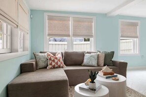 A living room with a sectional sofa, a round coffee table, and a window with blinds. - Beachside Bliss | 4BR (plus a bonus bedroom)  Folly Beach Home Steps from Beach Access (Folly Beach)