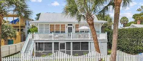A two-story house with a balcony, a covered porch, and a white picket fence.