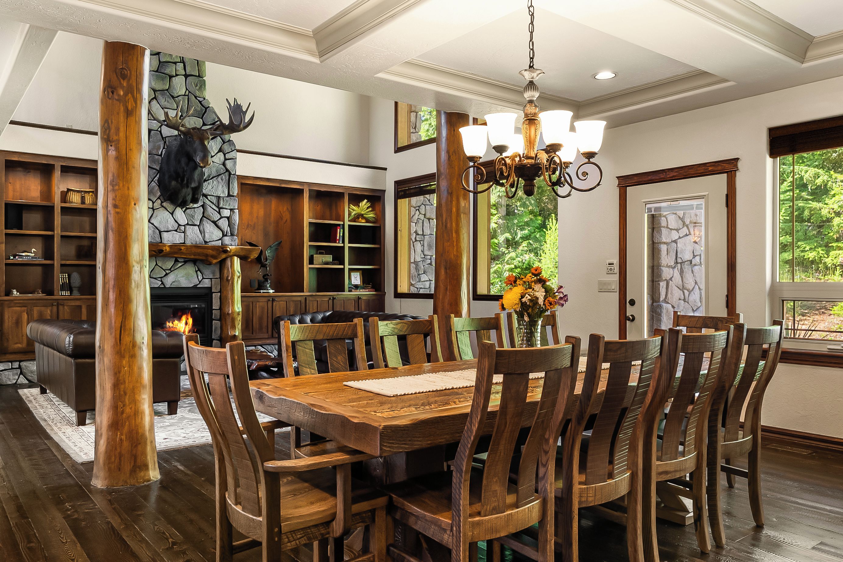Un comedor con una gran mesa de madera y sillas, una chimenea y una pared de piedra con una decoración de cabeza de oso.