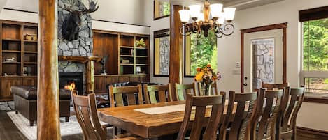 Un comedor con una gran mesa de madera y sillas, una chimenea y una pared de piedra con una decoración de cabeza de oso.