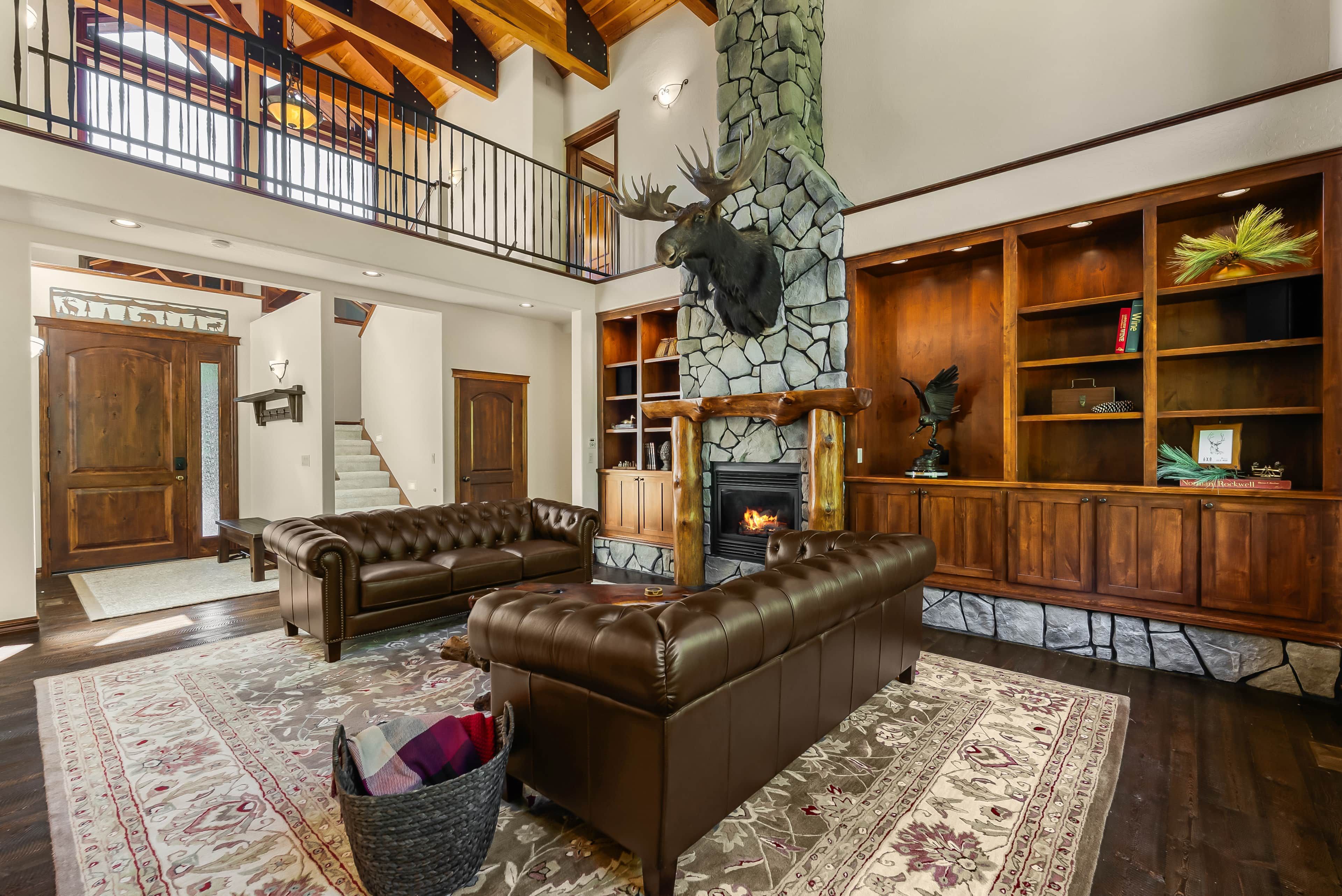 A spacious living room with leather sofas, a stone fireplace, and a wooden staircase.