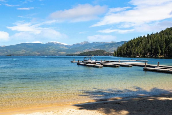 A clear lake with a dock and boats, surrounded by mountains and dense forest. - The Fairway Lodge - Priest Lake, ID (Priest Lake)