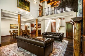 A spacious living area with a large leather sofa, a dining table with chairs, and a kitchen in the background. - The Fairway Lodge - Priest Lake, ID (Priest Lake)