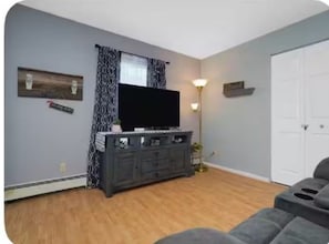 A living room with a flat-screen TV, dark-colored entertainment center, and a light floor lamp. - Graceful Stays: Cozy Highlands 1BR – Unit 6 (Louisville)