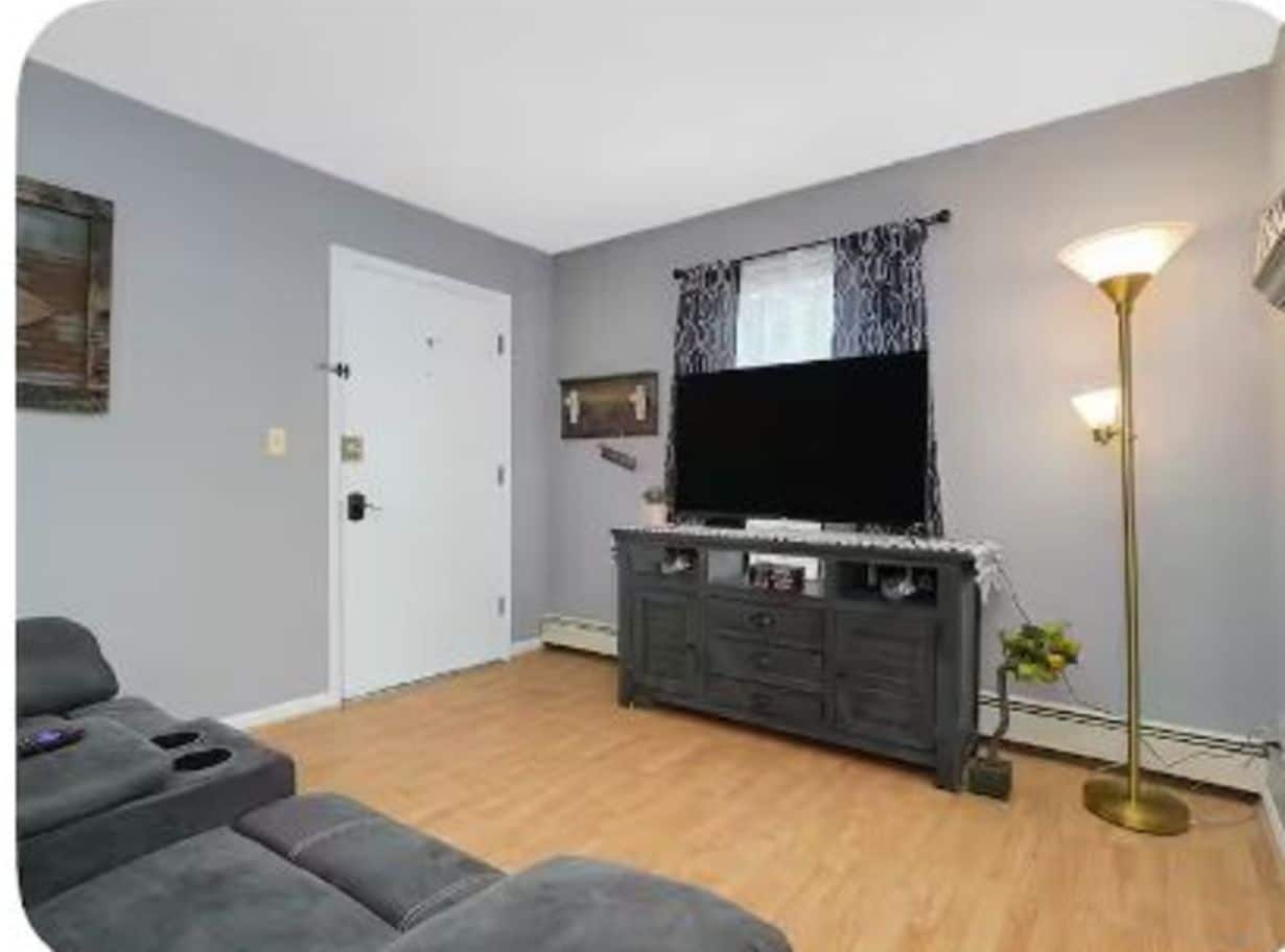 A living room with a flat-screen TV, dark-colored entertainment unit, and a floor lamp.