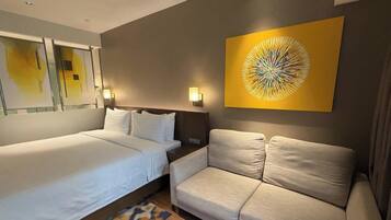 A hotel room with a bed, a sofa, and a wall-mounted artwork.
