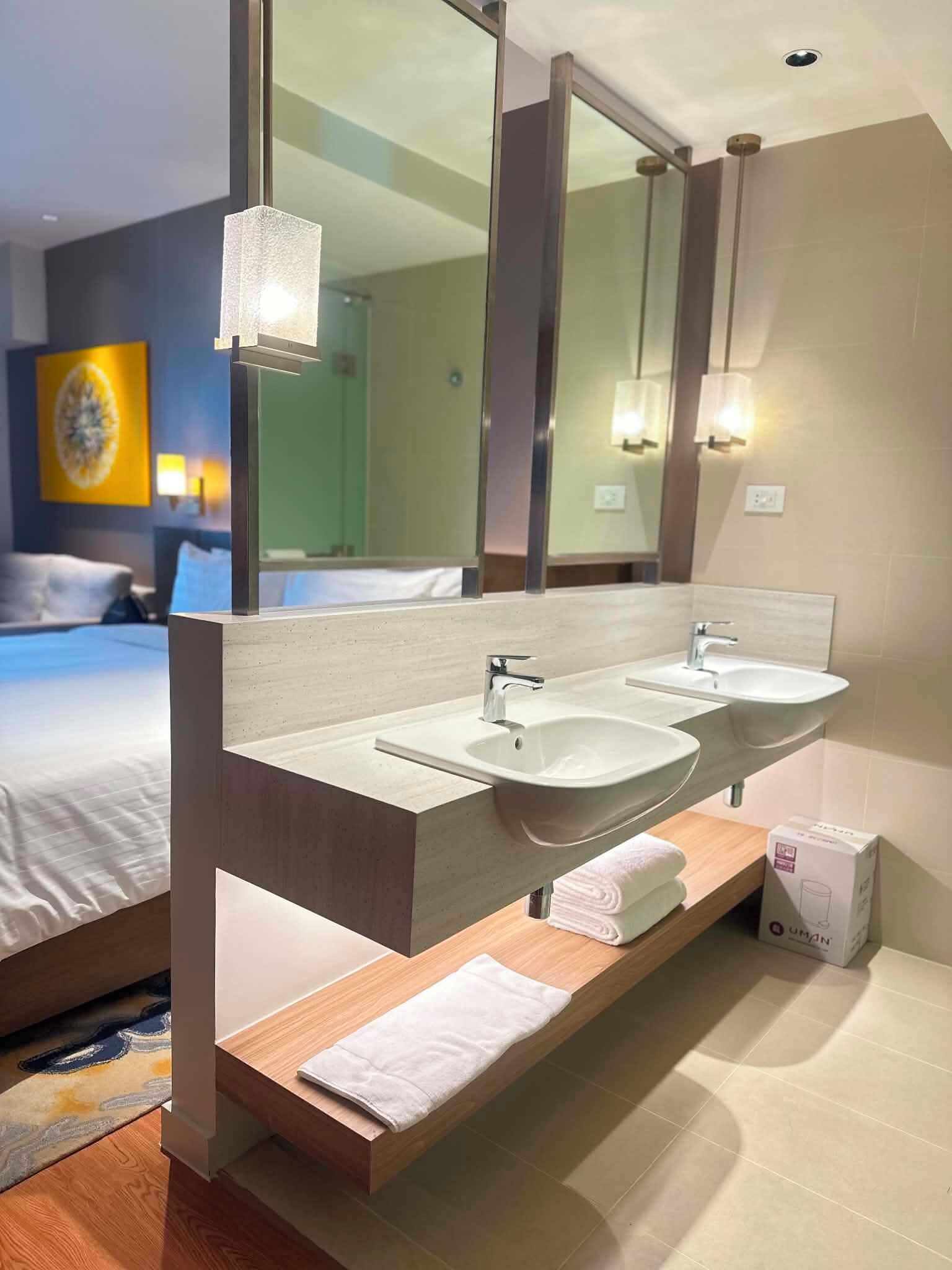 A hotel bathroom with a double sink, a large mirror, and a towel rack.