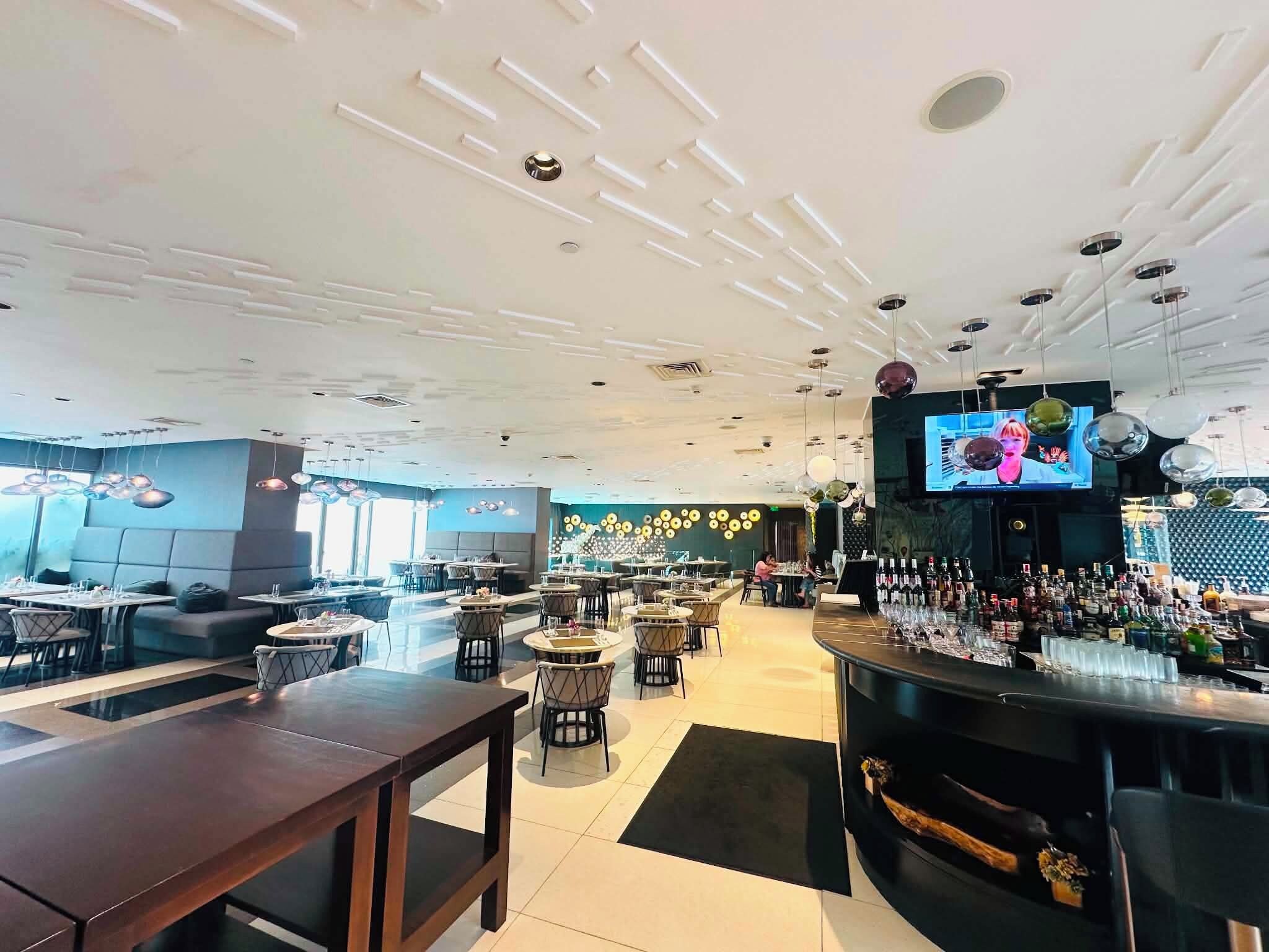 A modern bar area with a TV screen, seating arrangements, and a variety of bottles on the counter.
