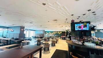 A modern bar area with a TV screen, seating arrangements, and a variety of bottles on the counter.