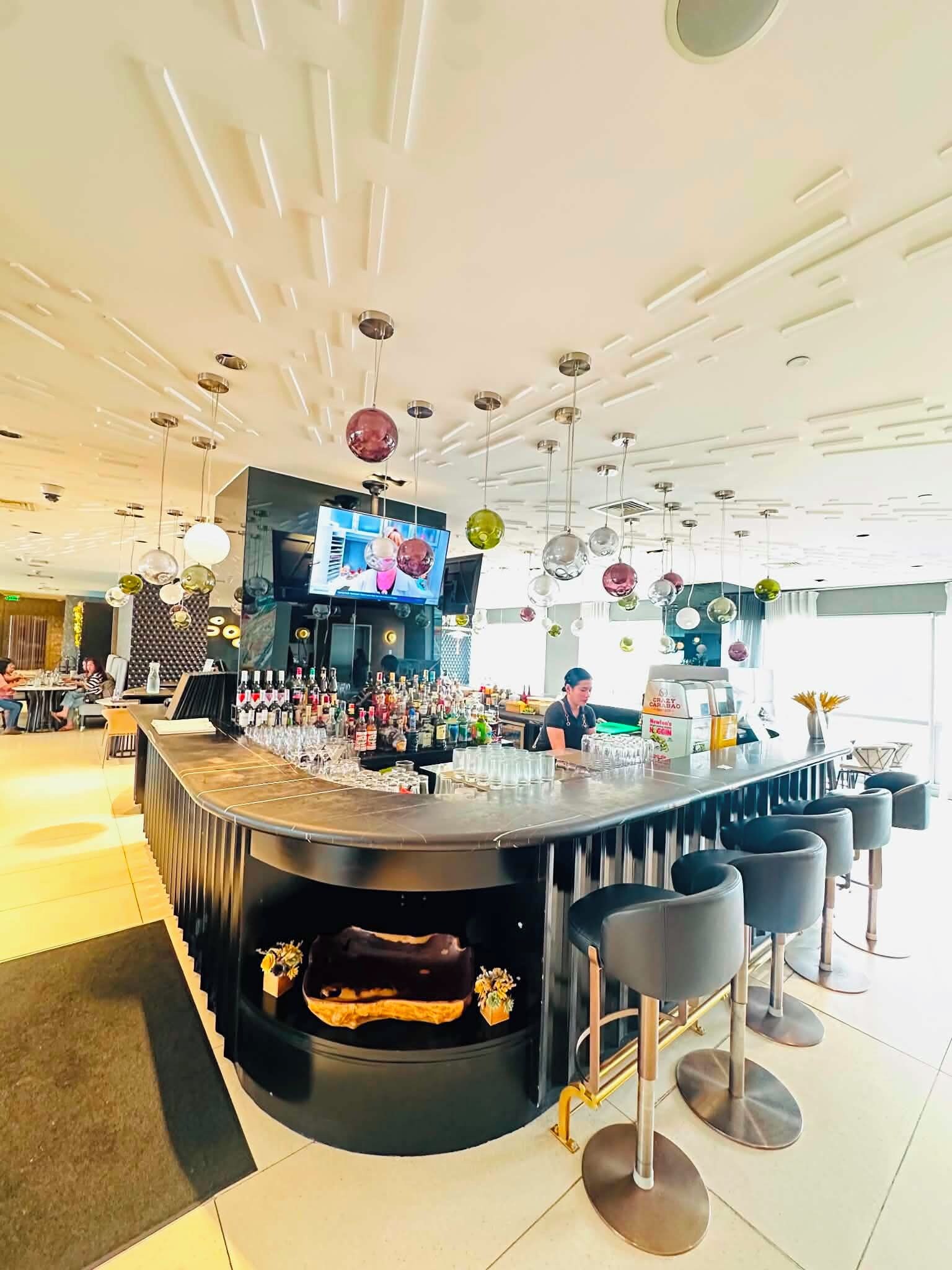 A bar area with a round counter, stools, and a variety of bottles.