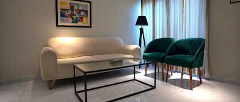 A living room with a sofa, two chairs, a glass coffee table, and a floor lamp.