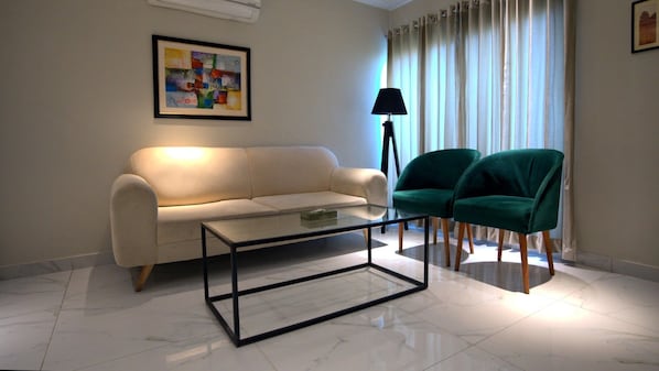 Ein Wohnzimmer mit einem weißen Sofa, einem Glastisch und zwei grünen Sessel.