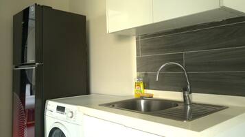 A kitchen with a stainless steel sink, a washing machine, and a refrigerator.