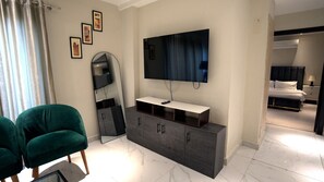 Ein modernes Hotelzimmer mit einem großen Flachbildfernseher an der Wand, einem grauen Schrank mit Spiegel und einem grünen Sessel.