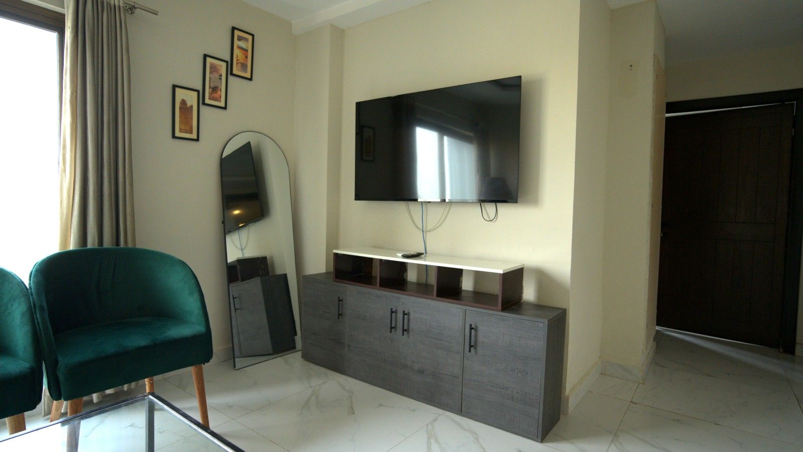 A modern living room with a flat-screen TV, a grey cabinet, a green armchair, and a large mirror.