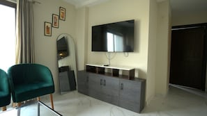 Una sala moderna con un televisor de pantalla plana, un mueble gris, un sillón verde y un espejo grande.