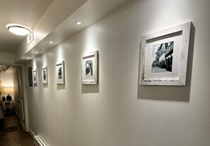 A hallway with framed photographs on the wall, a door at the end, and a staircase leading to another floor. - 1BR/1BA in Andersonville · pet-friendly · workspace · garage parking · king bed (Chicago)