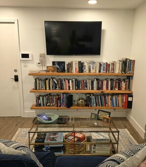 Ein Wohnzimmer mit Bücherregal, Flachbildfernseher und Couchtisch mit Büchern und Dekorationsobjekten.