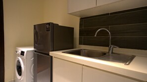 Eine kleine Küche mit einem Edelstahl-Kühlschrank, einer eingebauten Waschmaschine und einem modernen Waschbecken mit elegantem Wasserhahn.