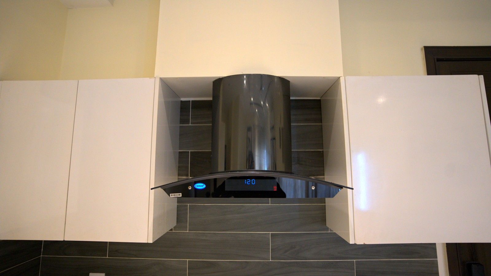 Cocina con campana de acero inoxidable, armarios blancos y piso de baldosas oscuras.