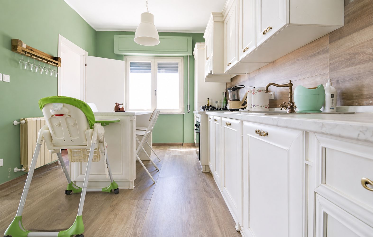 Une cuisine avec des meubles blancs, une chaise verte et une serpillière verte.