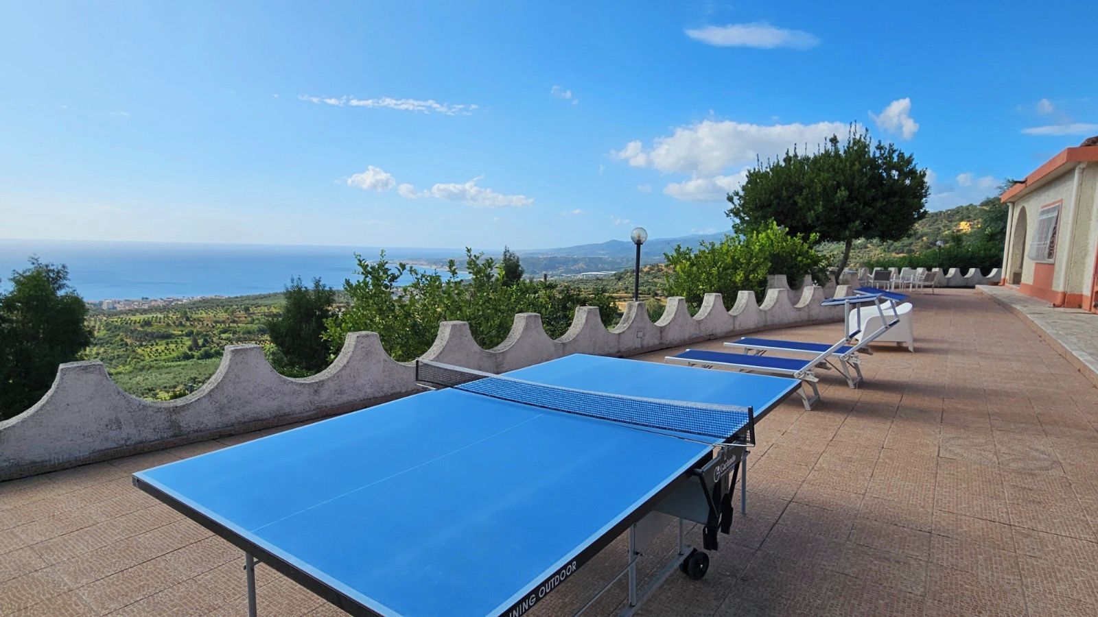 A ping pong table set up outdoors with a scenic view of the sea and hills in the background.