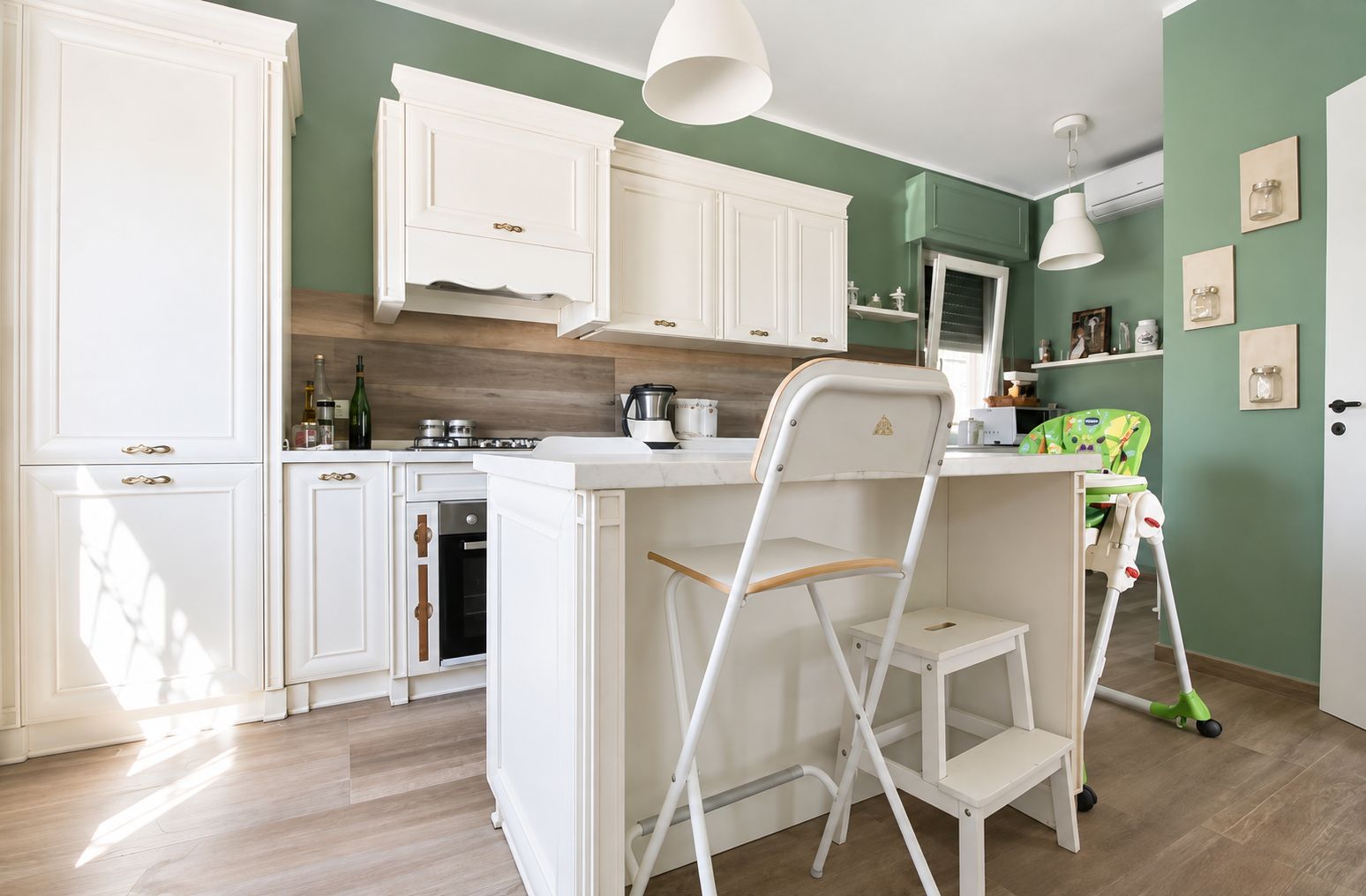 A kitchen with white cabinetry, a dining area with a high chair, and a green wall.