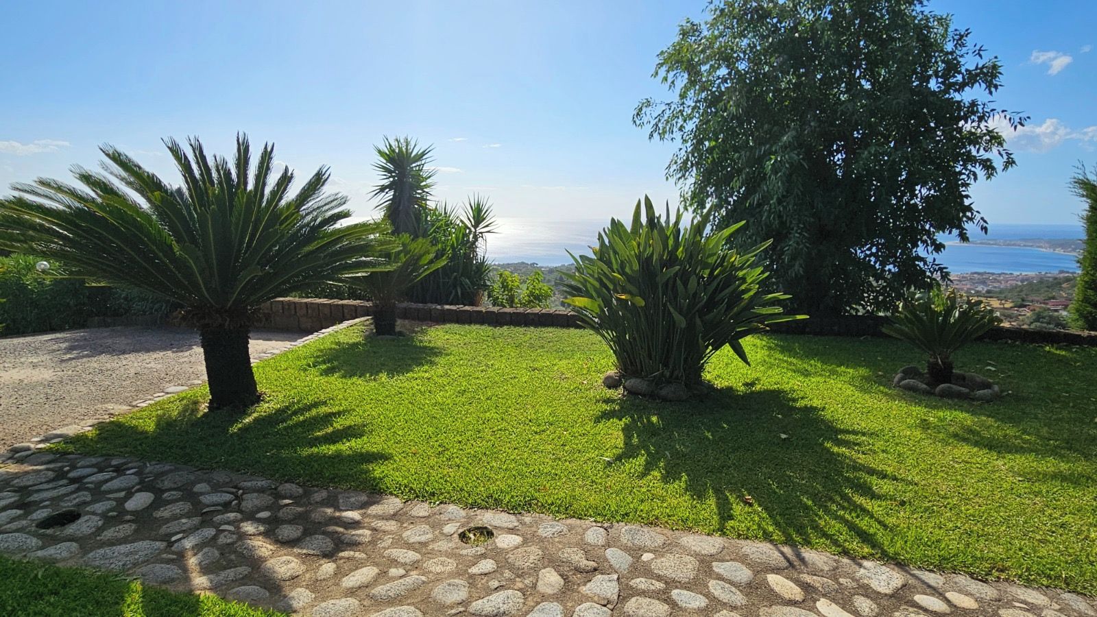 Un jardin aménagé avec un sentier en pierre, différents arbustes et une vue sur la mer.