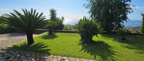 A landscaped garden with a stone pathway, various shrubs, and a view of the sea.