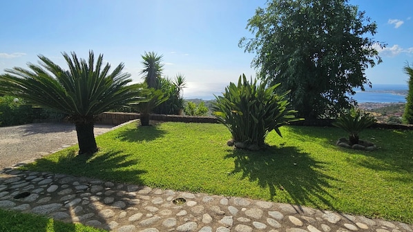 A landscaped garden with a stone pathway, various shrubs, and a view of the sea.