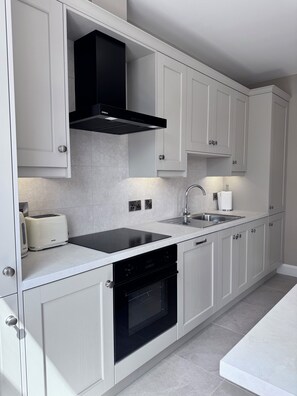 A modern kitchen with white cabinetry, a black range hood, a built-in dishwasher, and a stainless steel sink.