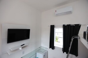 Een hotelkamer met een flatscreen televisie, een glazen kast, een raam met gordijnen en een airconditioning.