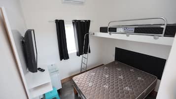 A bunk bed with a mattress labeled 'FireGuard,' a small desk with a chair, a television mounted on the wall, and a window with curtains.