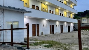 A multi-story building with a flat roof, multiple balconies, and a gravel courtyard. - A5 suites (Ubatuba)